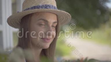 一个<strong>妩媚</strong>的年轻女子，戴着草帽，穿着白色连衣裙，坐在小村屋前。 农村